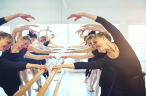 Cheerful,Mature,Ballerinas,Stretching,With,Hands,Up,Standing,At,Mirror
